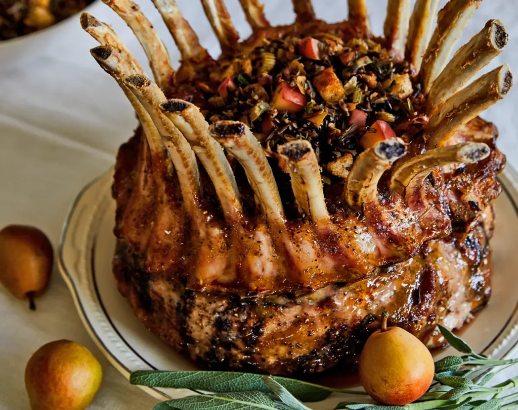 Anjou glazed crown roast pork topped with pear stuffing, roasted bones, fresh sage, and whole pears on a serving platter