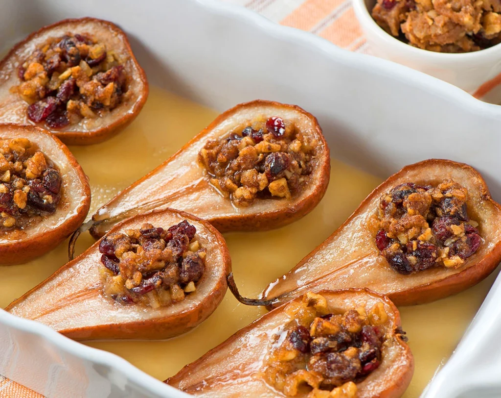 Baked stuffed pears filled with cranberries and walnuts in a white baking dish with honey syrup