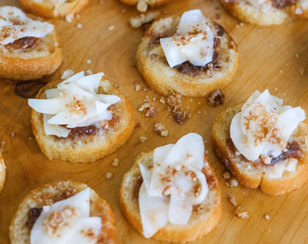 Bruschetta topped with balsamic fig jam, toasted bread rounds, and coconut flakes on a wooden board