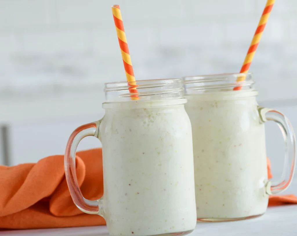 Creamy pear smoothie served in mason jars with striped paper straws on a white surface