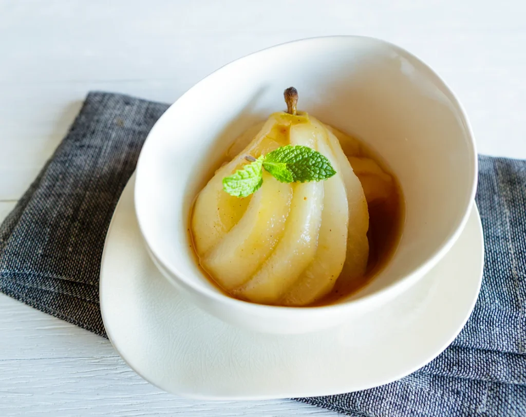 Spiced Anjou poached pear served in a white bowl with warm syrup and fresh mint garnish