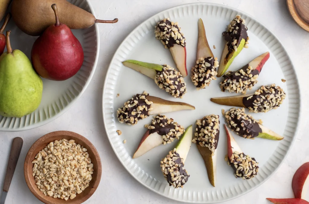 Chocolate- and walnut-coated pear slices arranged on a white plate.
