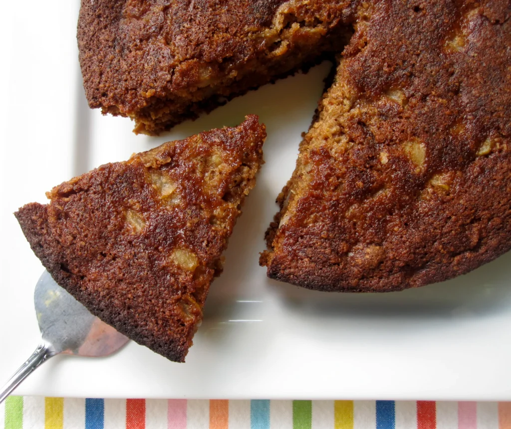 Pear oat and almond cake with a sliced wedge on a white serving plate.