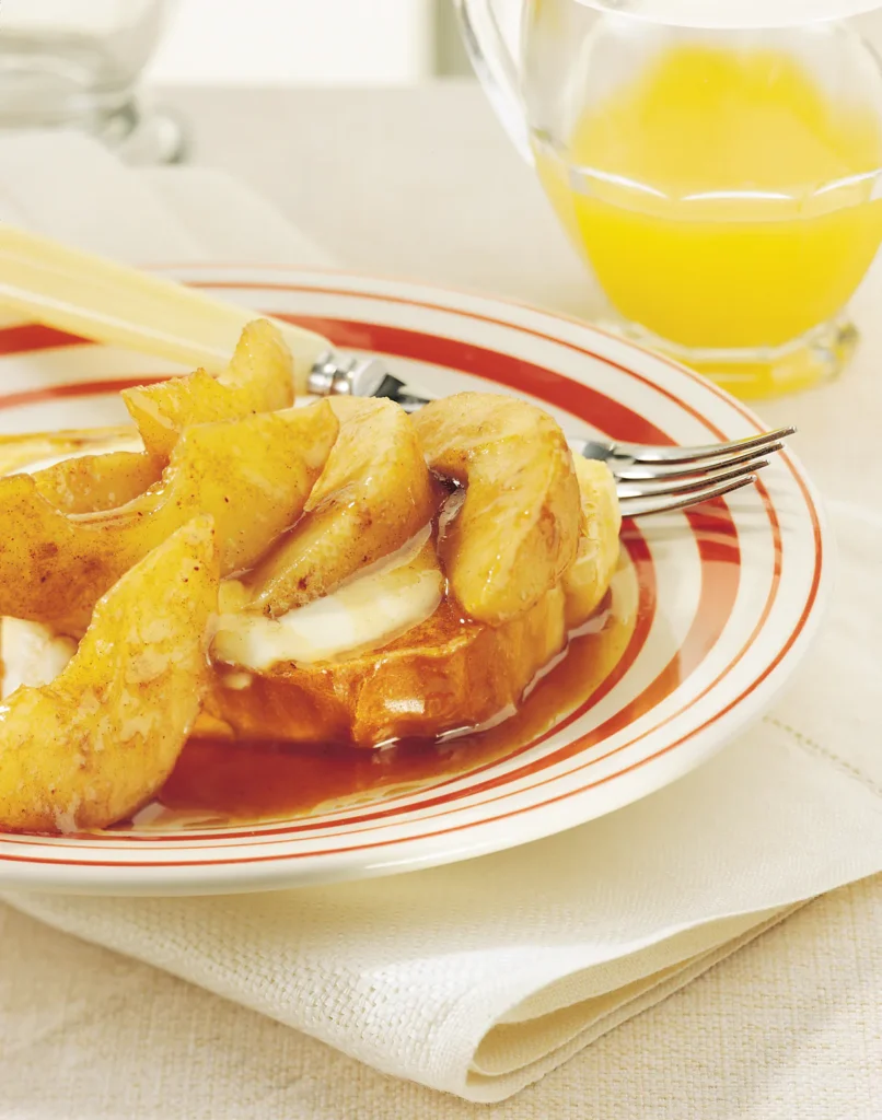 Maple-glazed pears served over French toast with syrup on a striped plate.