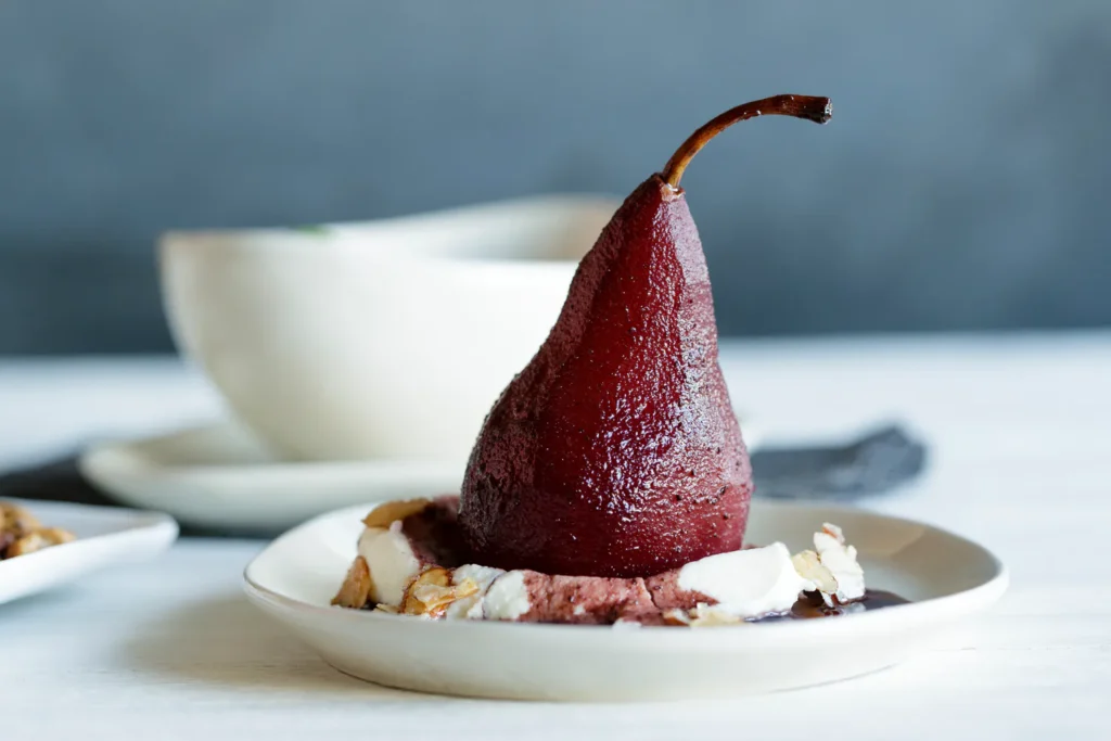 Red wine poached pear with mascarpone cream and candied almonds on a dessert plate.