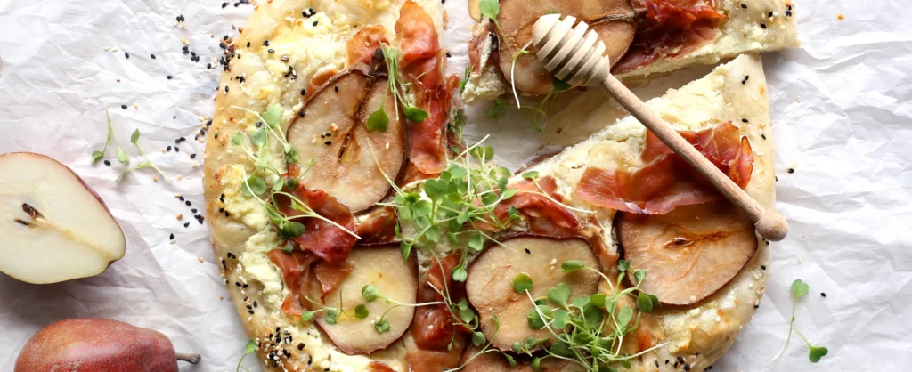 Grilled pear and prosciutto flatbread pizza with ricotta, microgreens, and honey drizzle.