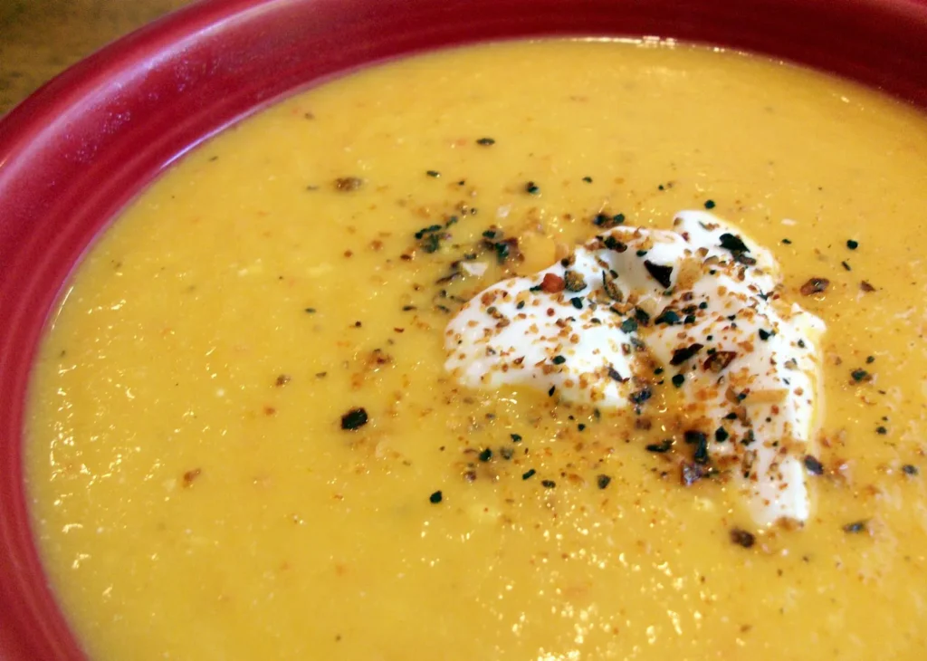Bowl of pumpkin pear pureed soup topped with a dollop of cream and cracked black pepper.