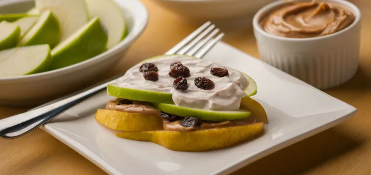 Fruit napoleon of pear and apple slices layered with peanut butter, yogurt and raisins on a white plate
