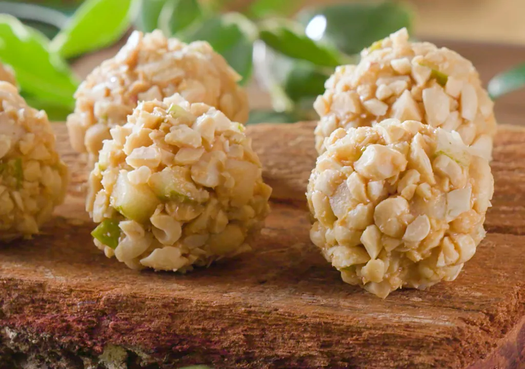 Pear and peanut dog treats rolled in chopped peanuts on a wooden board